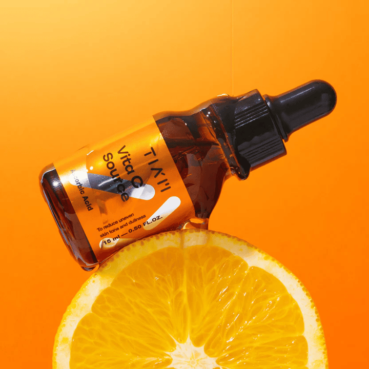 TIA'M Vita C Source-bouteille placée contre une orange et un fond orange symbolisant la fraîcheur et l'effet antioxydant de la vitamine C.