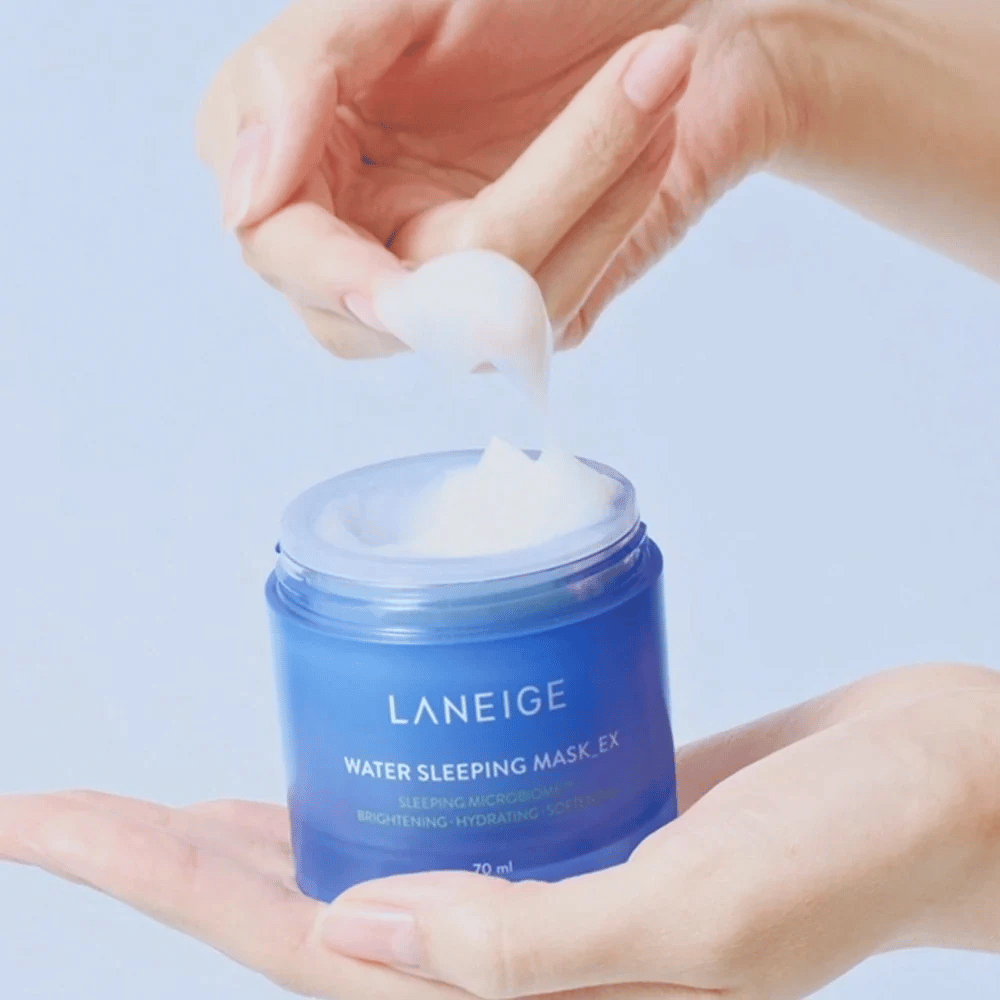 Une main prélève LANEIGE Water Sleeping Mask d'un pot bleu, en mettant l'accent sur la consistance gélatineuse sur fond bleu clair.