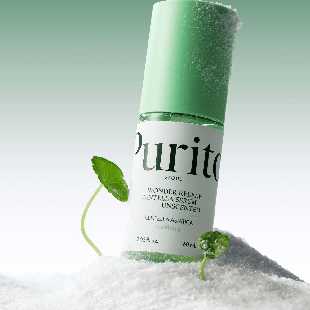 Bouteille avec Purito Sérum Centella est dans la neige, des feuilles vertes sont visibles, sur un fond vert doux.