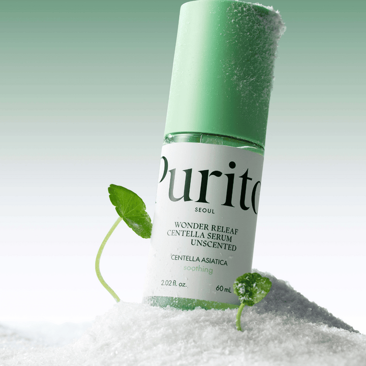 Bouteille avec Purito Sérum Centella est dans la neige, des feuilles vertes sont visibles, sur un fond vert doux.
