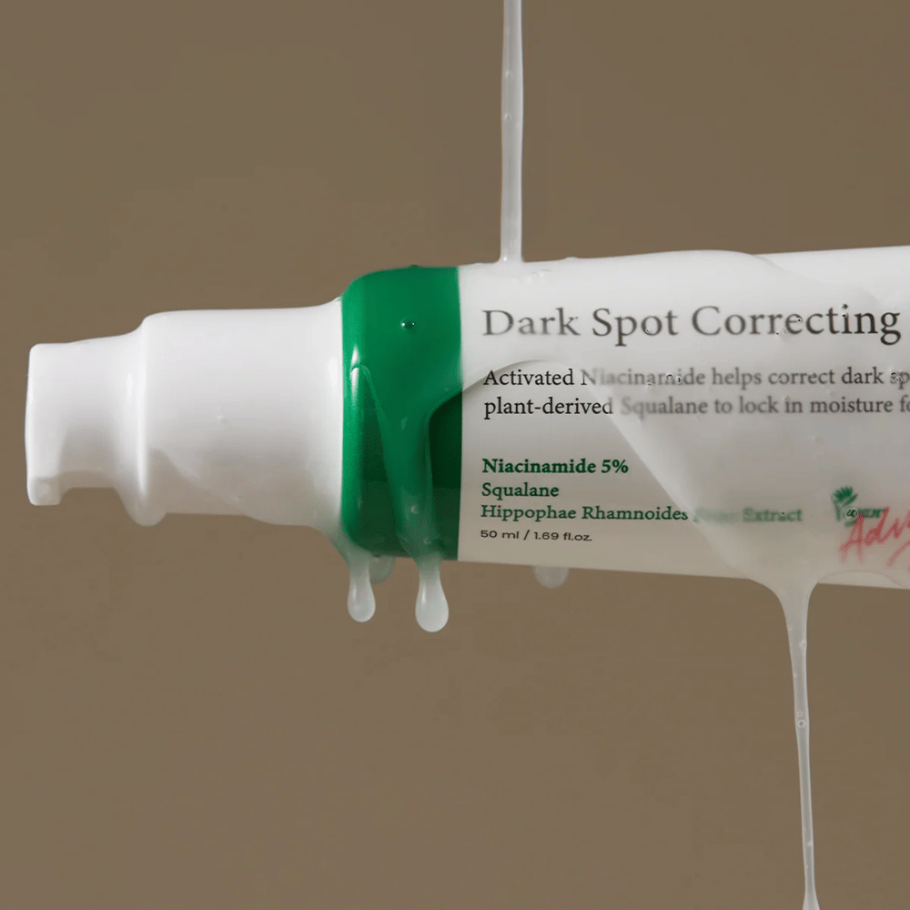 Gros plan sur un flacon pompe de Axis-Y Dark Spot Correcting Glow Serum avec emballage blanc et bouchon vert, recouvert de liquide transparent coulant.