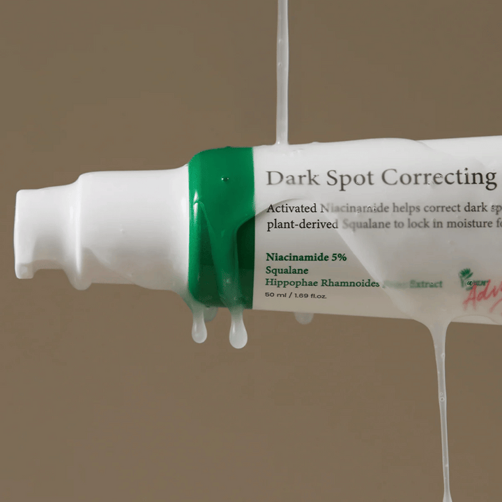 Gros plan sur un flacon pompe de Axis-Y Dark Spot Correcting Glow Serum avec emballage blanc et bouchon vert, recouvert de liquide transparent coulant.