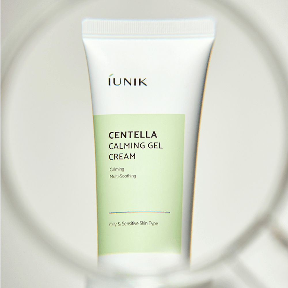 Un tube iUNIK Centella Calming Gel Cream avec un design blanc et vert clair est debout, vu à travers un cadre rond ressemblant à une loupe.
