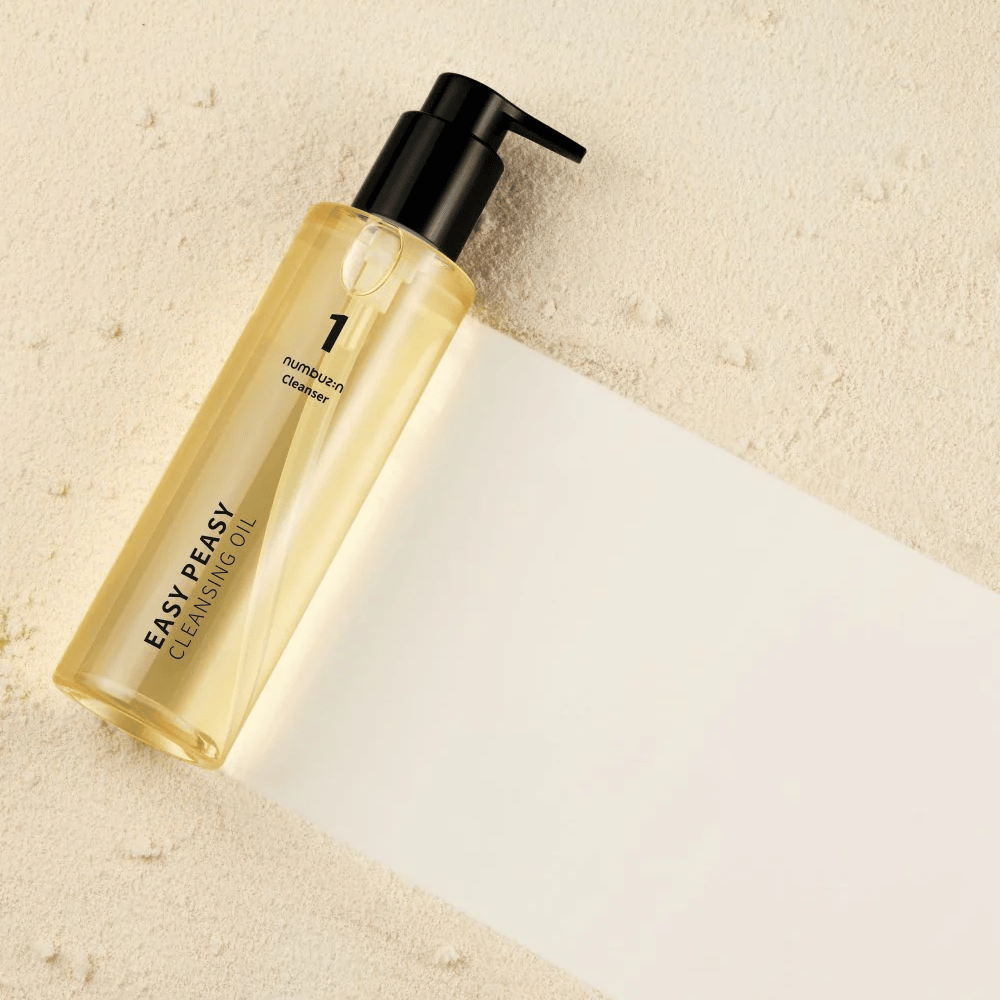Numbuzin No.1 Easy Peasy Cleansing Oil allongé sur une surface couleur sable avec ombre.