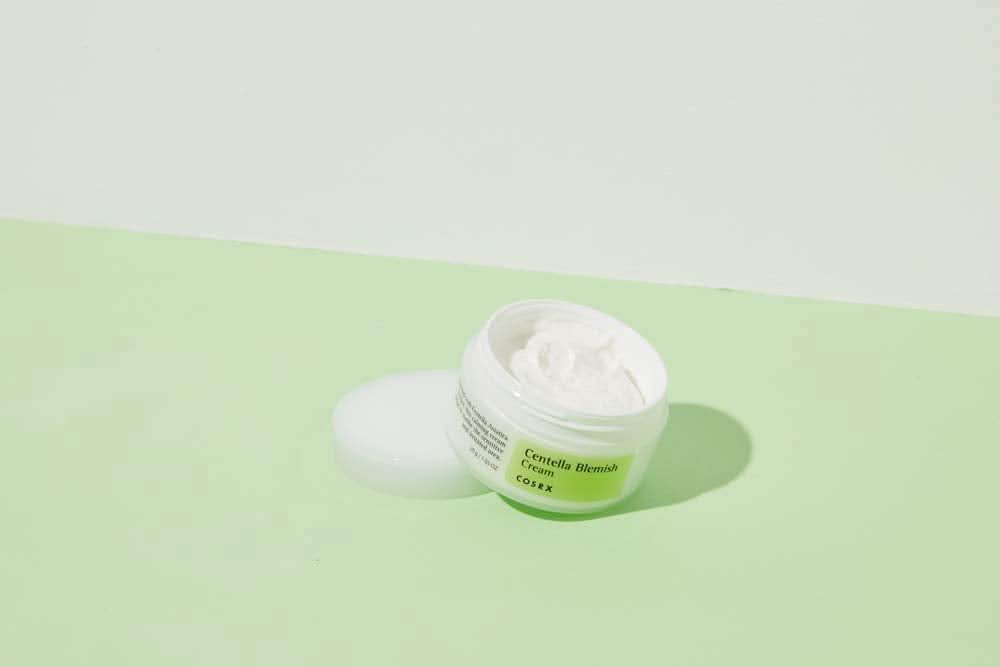 Un pot de COSRX Centella Blemish Cream 30ml posé sur une surface verte.