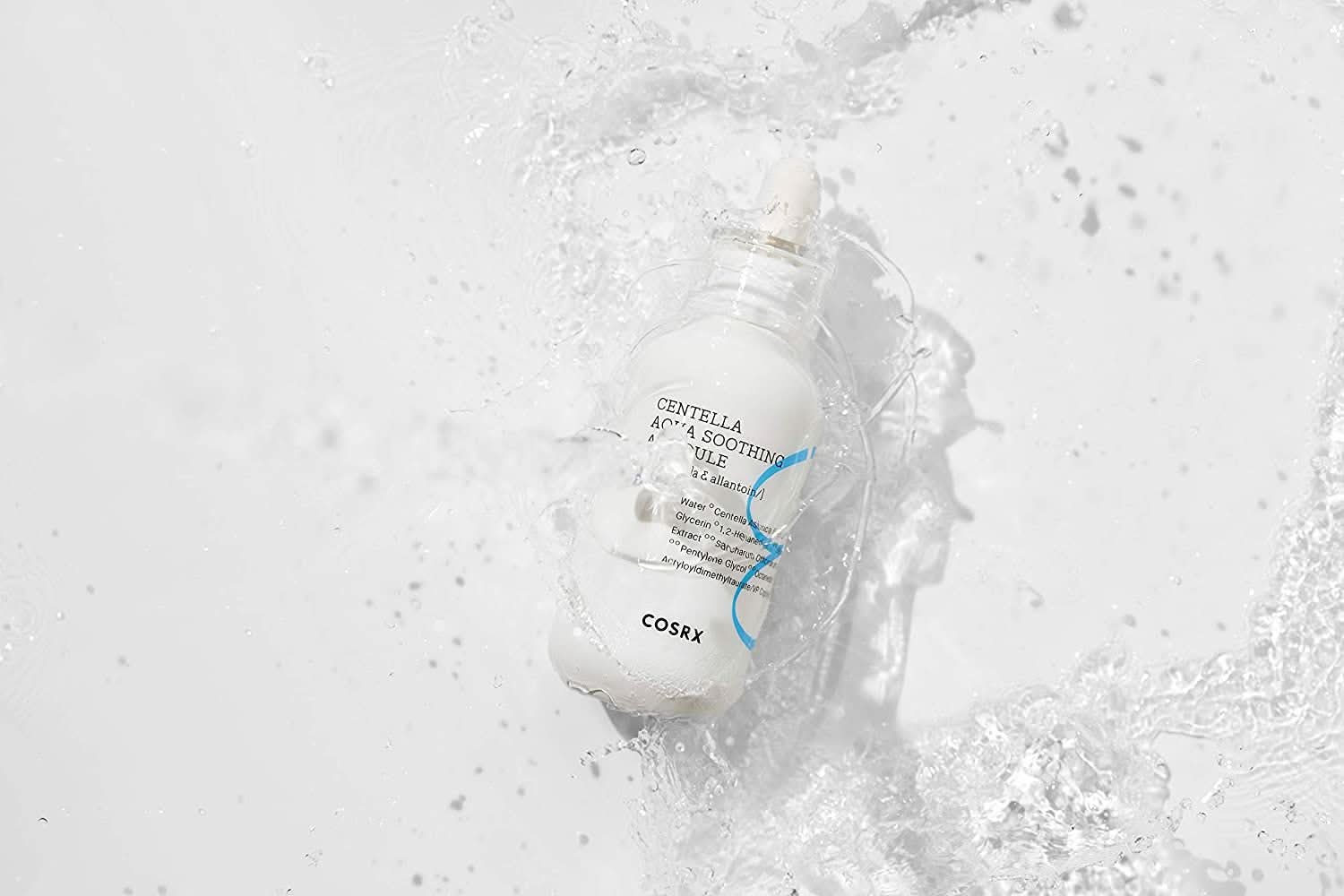 Une bouteille COSRX Centella Aqua Soothing Ampoule 40ml qui éclabousse sur une surface blanche, réduit les rougeurs et offre une hydratation apaisante.