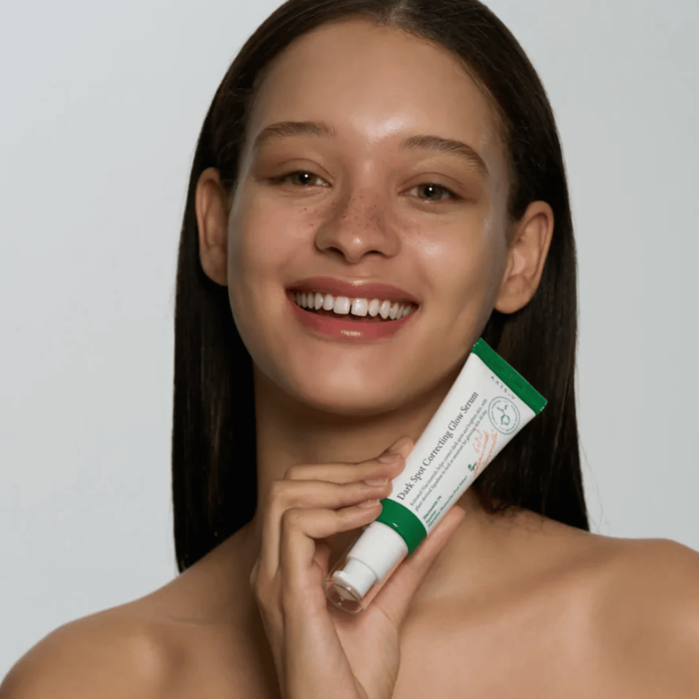Une jeune femme tient un tube de AXIS - Y Dark Spot Correcting Glow Serum 50ml.