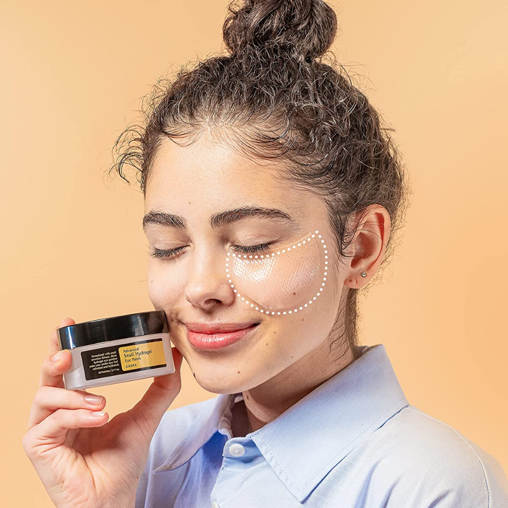 Une femme tenant un pot COSRX Advanced Snail Hydrogel Eye Patch 60 pièces de crème pour le visage.
