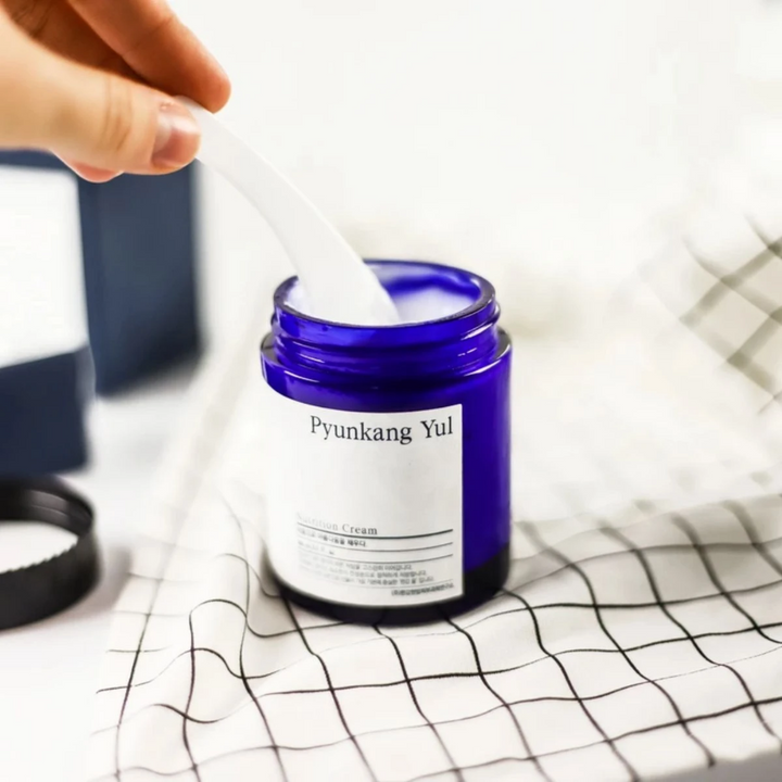 Une personne utilise un pot Pyunkang Yul Nutrition Cream 100ml sur une table.