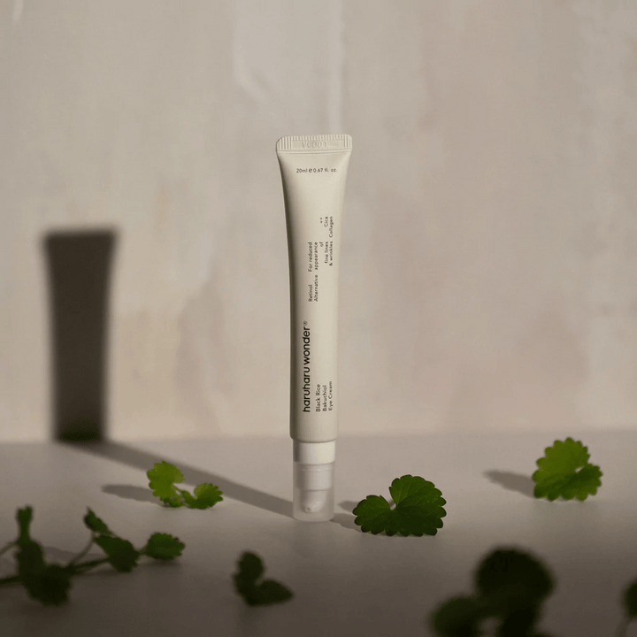 Un tube Haruharu Wonder Black Rice Bakuchiol Eye Cream 20ml entouré de feuilles vertes, axé sur la visibilité des rides et des ridules.
