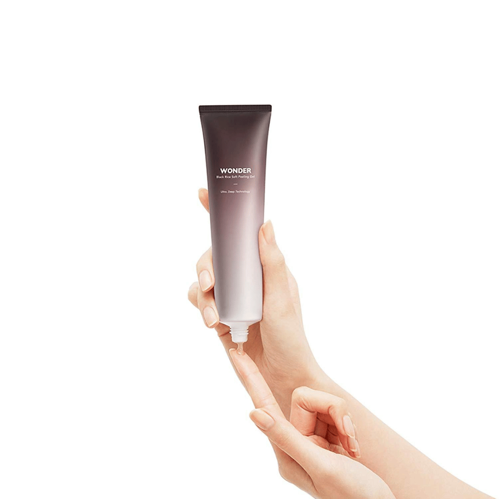 Une main de femme tenant un tube Haruhuru Wonders Black Rice Soft Peeling Gel 100 ml sur un fond blanc.