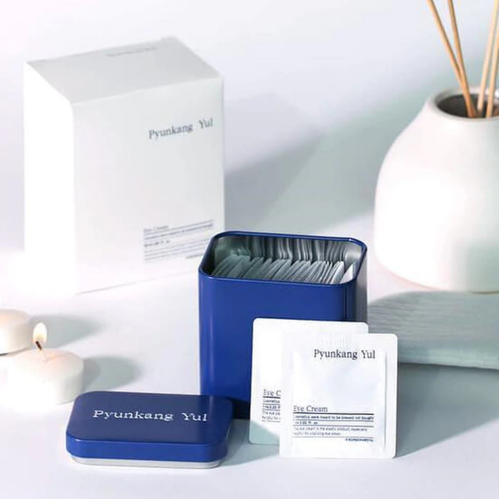 Une boîte blanche avec un couvercle bleu et Pyunkang Yul Crème pour les yeux 1ml x 50pcs à côté.