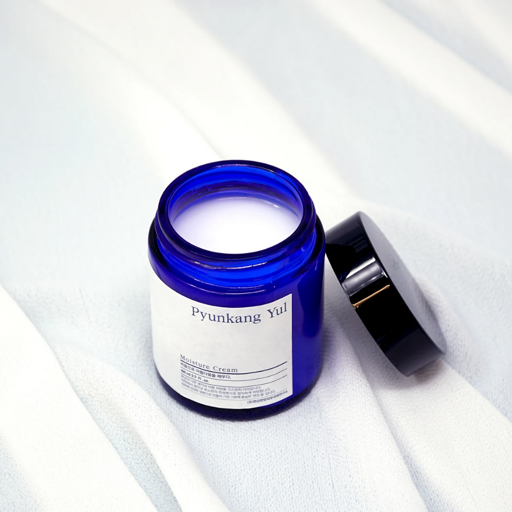 Un pot bleu avec un couvercle posé sur un tissu blanc montrant les propriétés hydratantes de Pyunkang Yul's Moisture Cream 100ml.