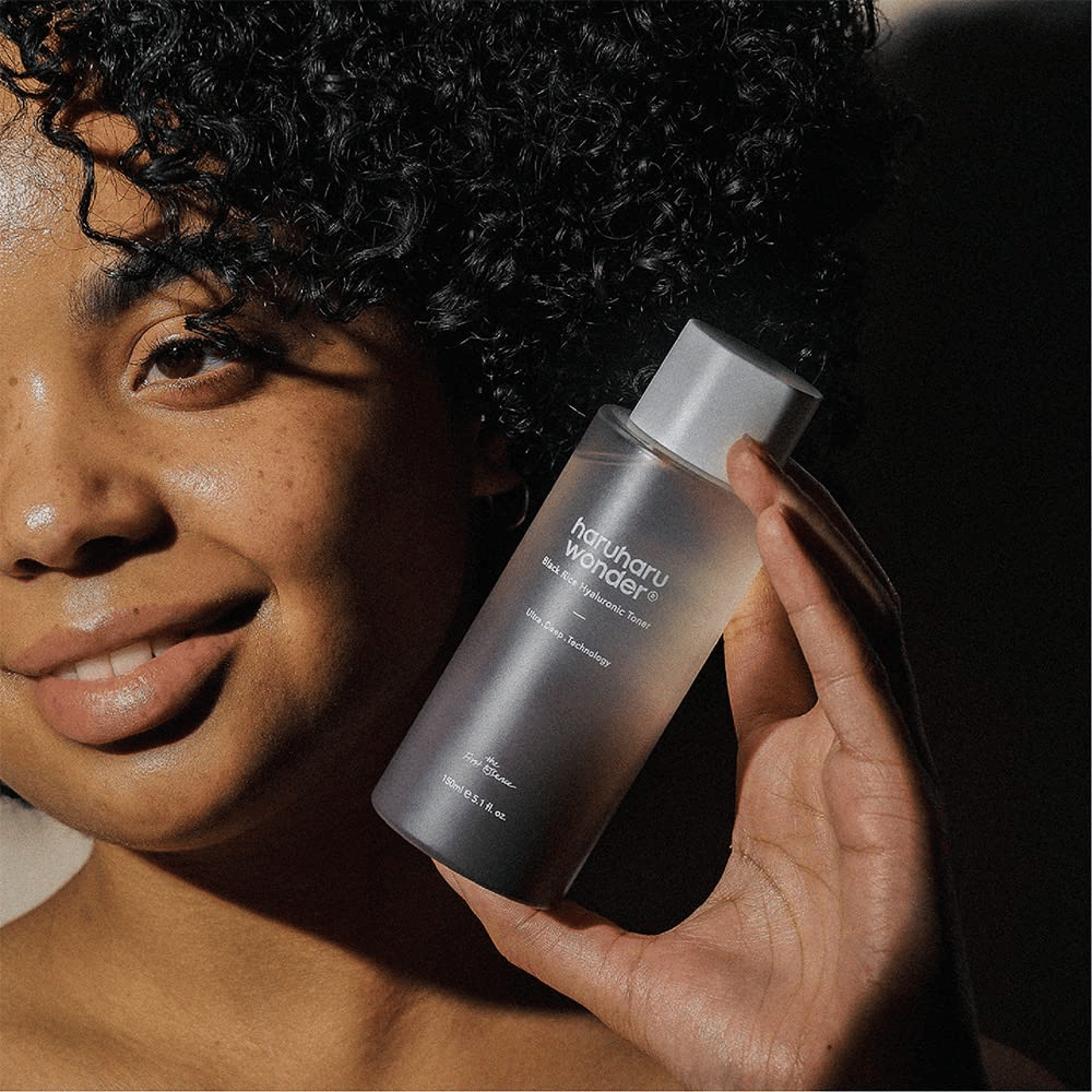 Une femme tenant une bouteille de Haruharu Wonder Black Rice Hyaluronic Toner Original 150ml.