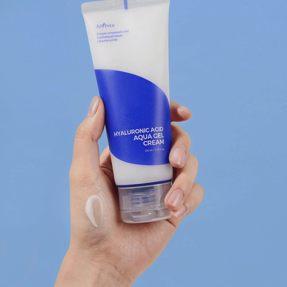 Une main tenant un tube Isntree Hyaluronic Acid Aqua Gel Cream 100ml sur un fond bleu.